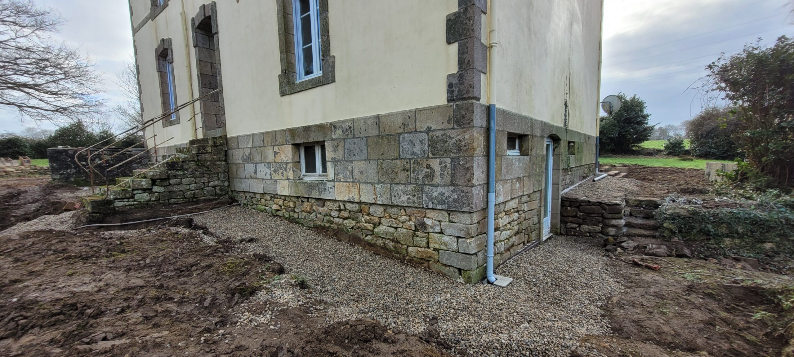 Façade en pierre avec soubassement et drainage en gravier.
