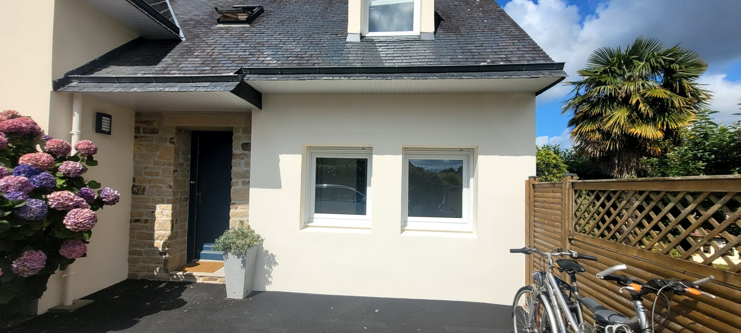 Façade d'une maison blanche avec fenêtres, fleurs et vélos.