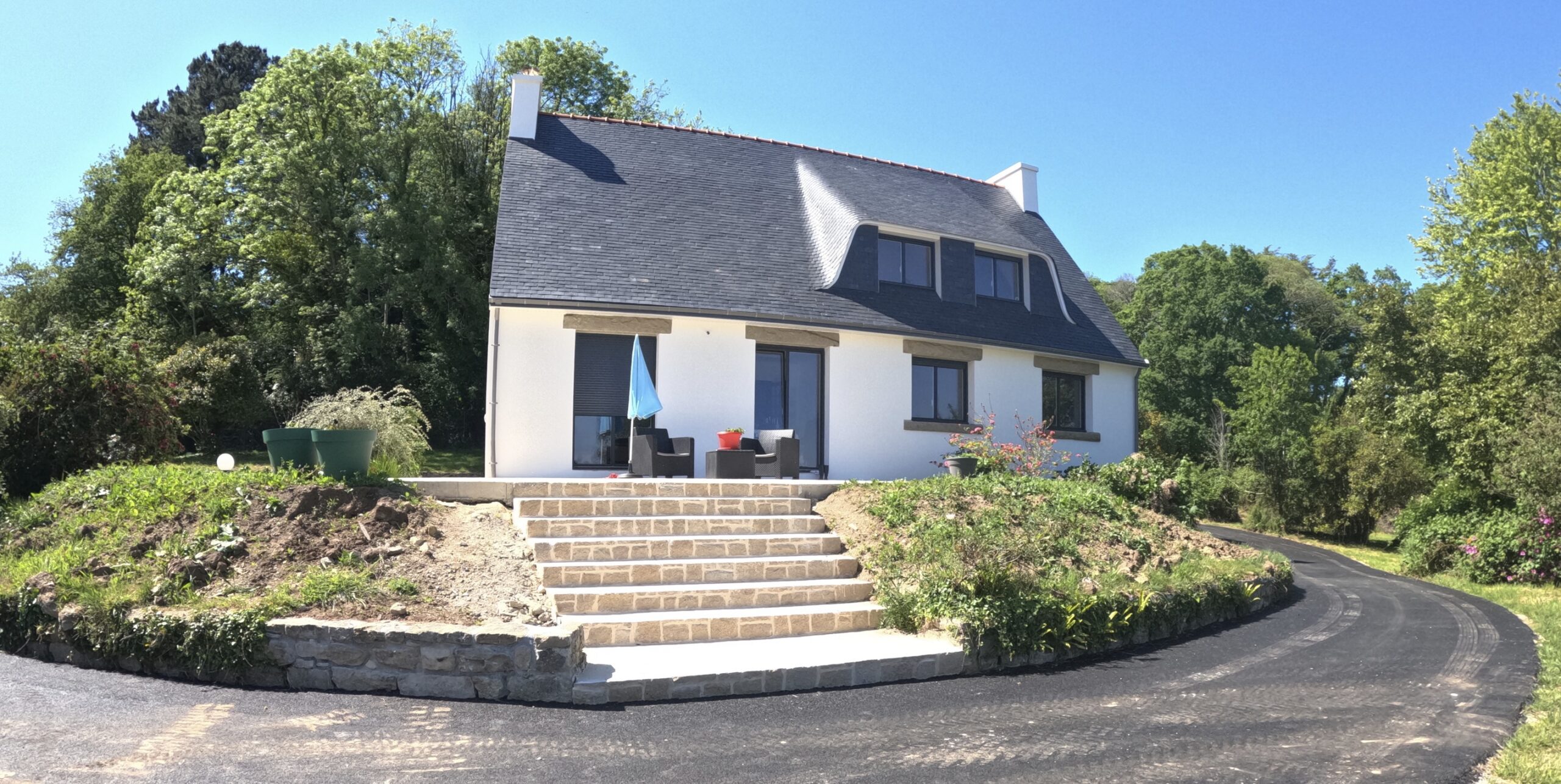 Maison blanche moderne avec toit en ardoise et escalier.