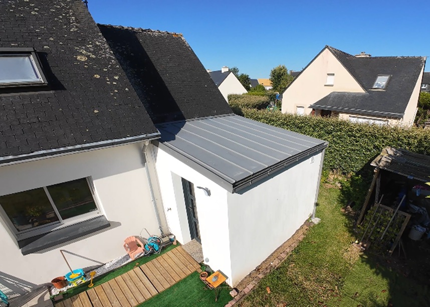Extension de maison blanche avec toit en zinc gris.